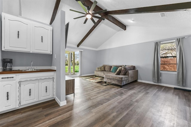 living room with sink, ceiling fan, vaulted ceiling with beams, a textured ceiling, and dark hardwood / wood-style flooring