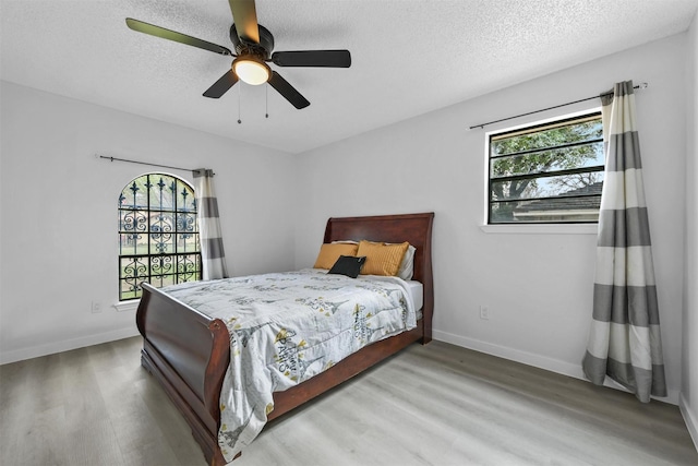 bedroom with multiple windows, a textured ceiling, ceiling fan, and light hardwood / wood-style flooring