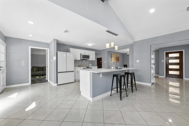 kitchen featuring vaulted ceiling, decorative light fixtures, white cabinetry, a breakfast bar area, and white refrigerator