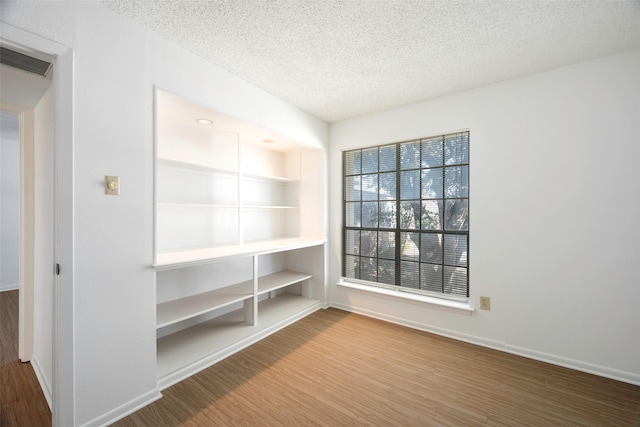 unfurnished room featuring hardwood / wood-style flooring, built in features, and a textured ceiling