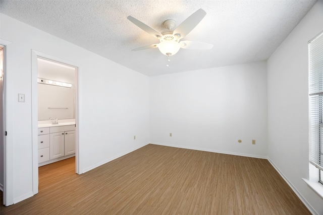 unfurnished bedroom featuring sink, ensuite bath, ceiling fan, a textured ceiling, and light wood-type flooring