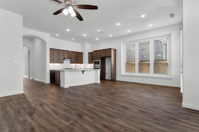 kitchen with a breakfast bar, stainless steel microwave, dark hardwood / wood-style flooring, a kitchen island with sink, and ceiling fan