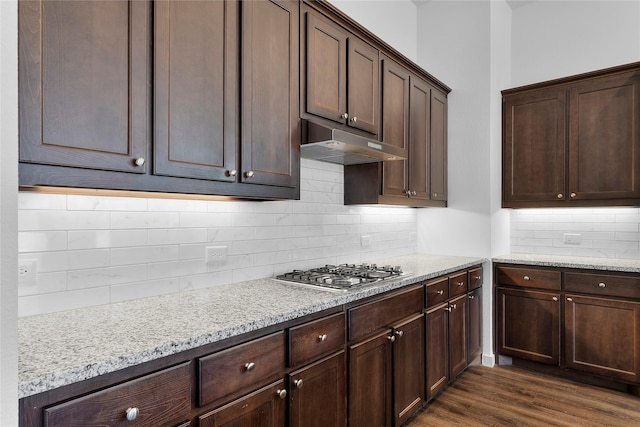 kitchen featuring dark brown cabinets, dark hardwood / wood-style floors, light stone counters, stainless steel gas cooktop, and decorative backsplash