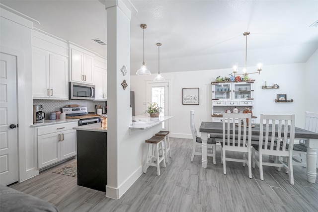 kitchen with decorative light fixtures, white cabinetry, a kitchen bar, stainless steel appliances, and light hardwood / wood-style flooring