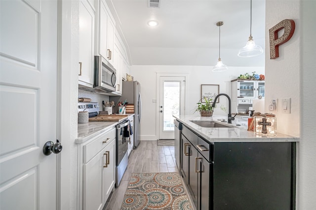 kitchen with appliances with stainless steel finishes, decorative light fixtures, sink, white cabinets, and light stone counters