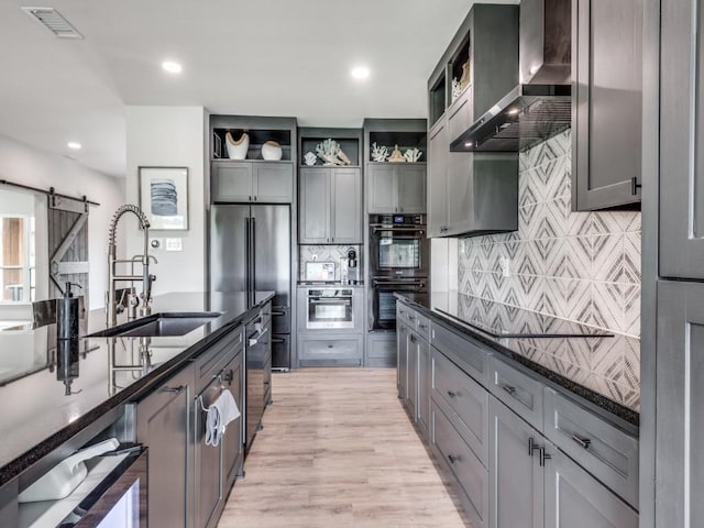 kitchen with wall chimney exhaust hood, sink, double oven, dark stone counters, and a barn door