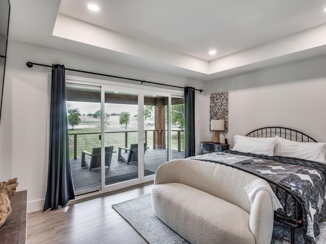 bedroom featuring access to exterior, light hardwood / wood-style flooring, and a raised ceiling