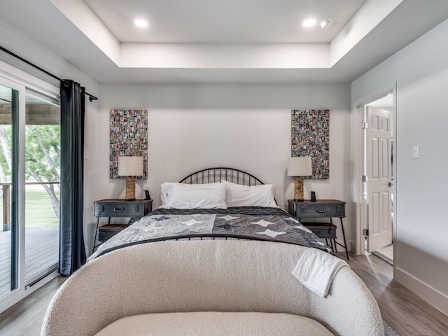 bedroom featuring wood-type flooring, access to exterior, and a tray ceiling