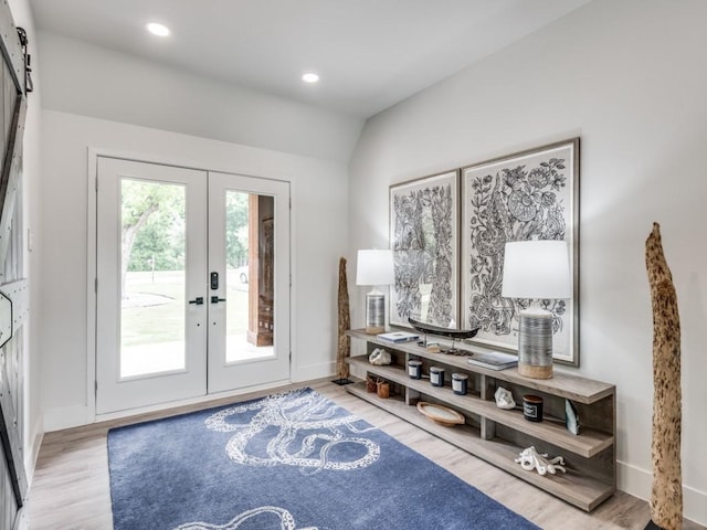 foyer entrance with vaulted ceiling, a barn door, light wood-type flooring, and french doors