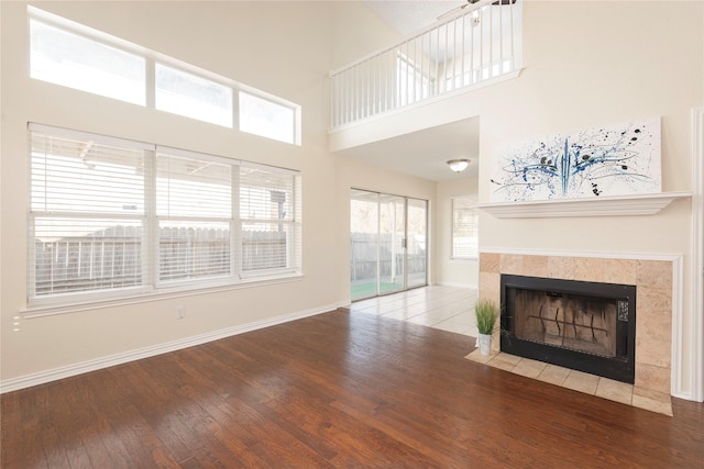 unfurnished living room with hardwood / wood-style floors, a tile fireplace, and a high ceiling