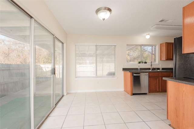 kitchen featuring sink, light tile patterned floors, stainless steel dishwasher, and black fridge