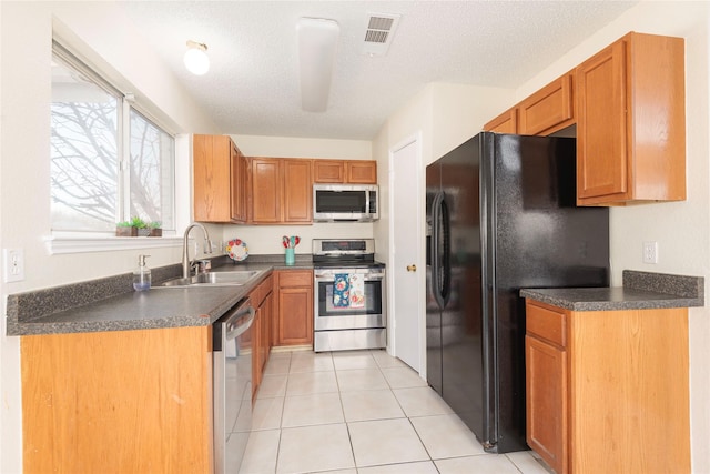 kitchen with light tile patterned flooring, appliances with stainless steel finishes, sink, and a textured ceiling