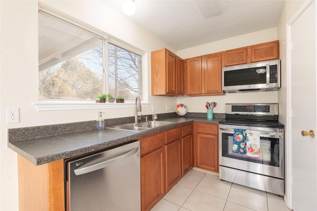 kitchen with sink, light tile patterned floors, ceiling fan, stainless steel appliances, and a textured ceiling