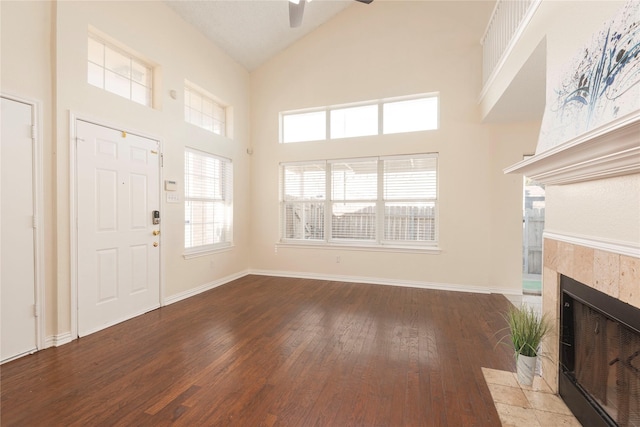 unfurnished living room featuring hardwood / wood-style floors, a tile fireplace, high vaulted ceiling, and ceiling fan