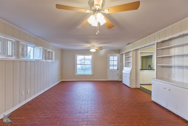 empty room with crown molding, a healthy amount of sunlight, wood walls, and built in shelves