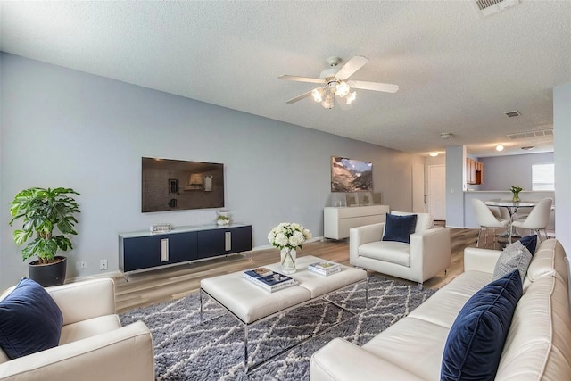 living room with wood finished floors, a textured ceiling, a ceiling fan, and visible vents