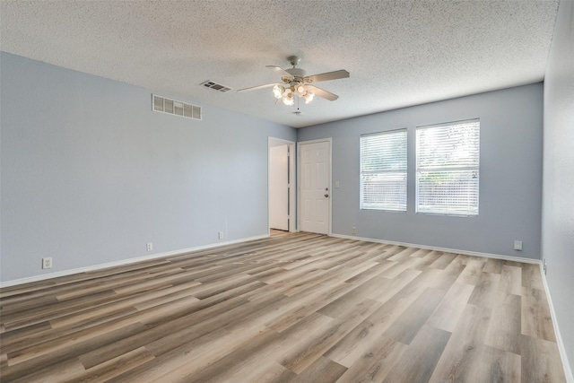empty room featuring ceiling fan, wood finished floors, visible vents, and a textured ceiling