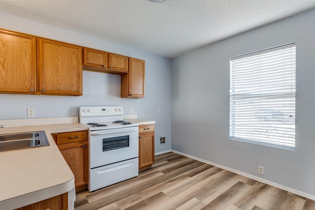 kitchen with white range with electric stovetop, a sink, a textured ceiling, light countertops, and light wood-style flooring