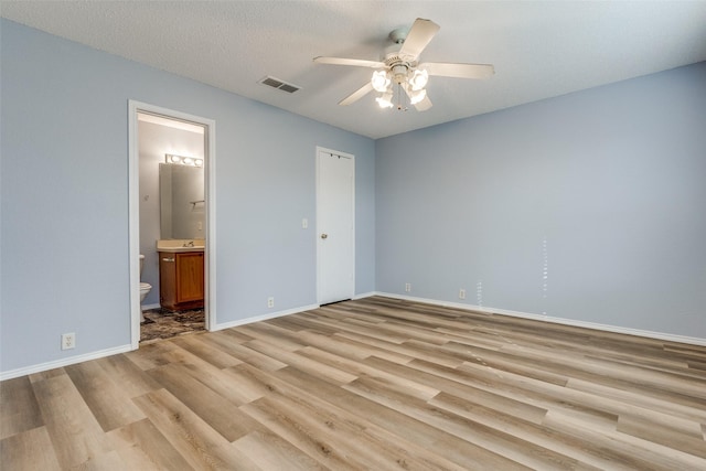 unfurnished bedroom with a ceiling fan, light wood-style floors, baseboards, ensuite bath, and visible vents