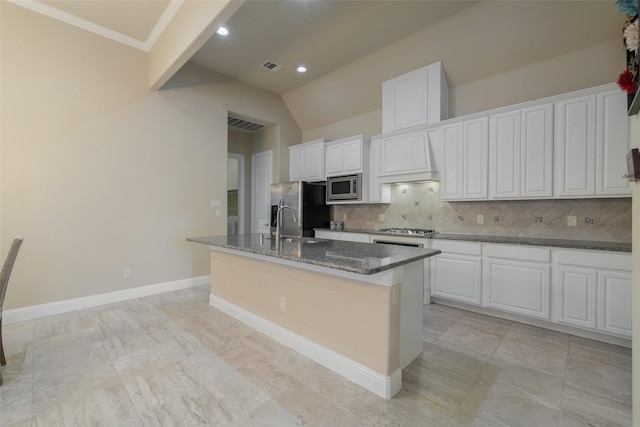 kitchen with white cabinetry, vaulted ceiling, a center island with sink, dark stone counters, and stainless steel appliances