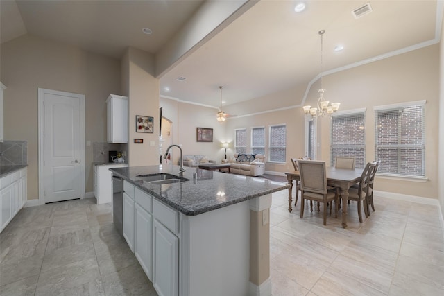 kitchen featuring pendant lighting, an island with sink, sink, white cabinets, and dark stone counters