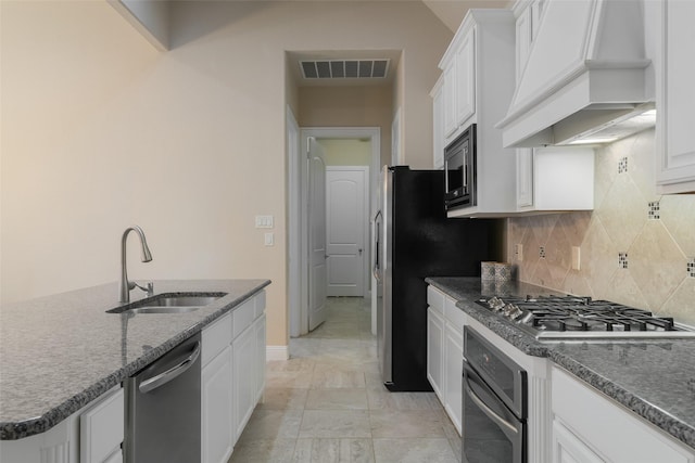 kitchen with sink, custom exhaust hood, dark stone countertops, appliances with stainless steel finishes, and white cabinets