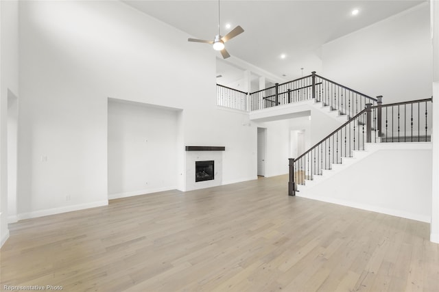 unfurnished living room with stairway, wood finished floors, baseboards, ceiling fan, and a tile fireplace