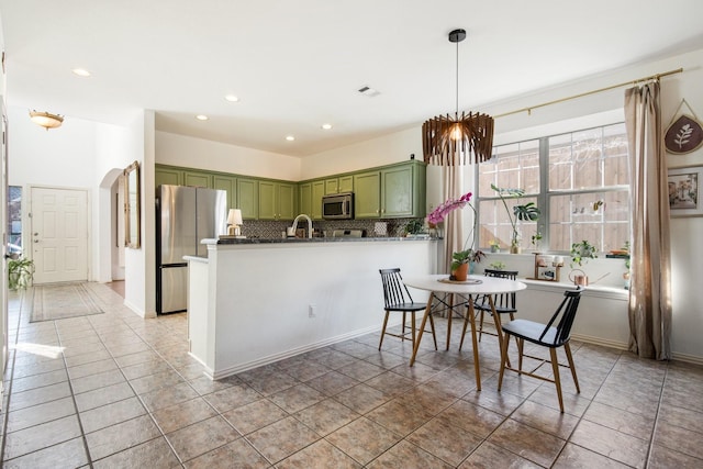 kitchen with tasteful backsplash, green cabinetry, tile patterned flooring, kitchen peninsula, and stainless steel appliances