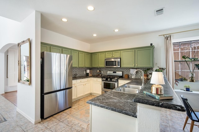 kitchen with sink, appliances with stainless steel finishes, backsplash, green cabinetry, and kitchen peninsula