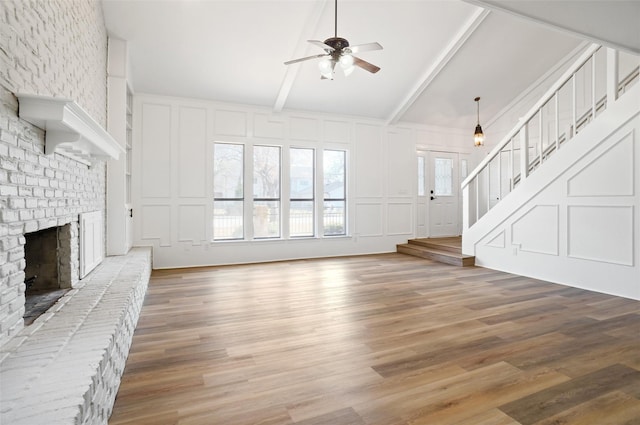 unfurnished living room with ceiling fan, a fireplace, vaulted ceiling with beams, and wood-type flooring