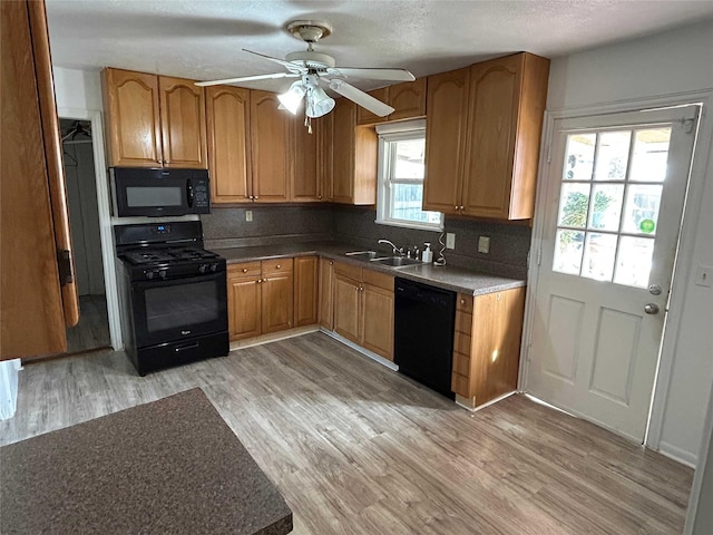 kitchen with black appliances, light wood finished floors, brown cabinetry, and a sink