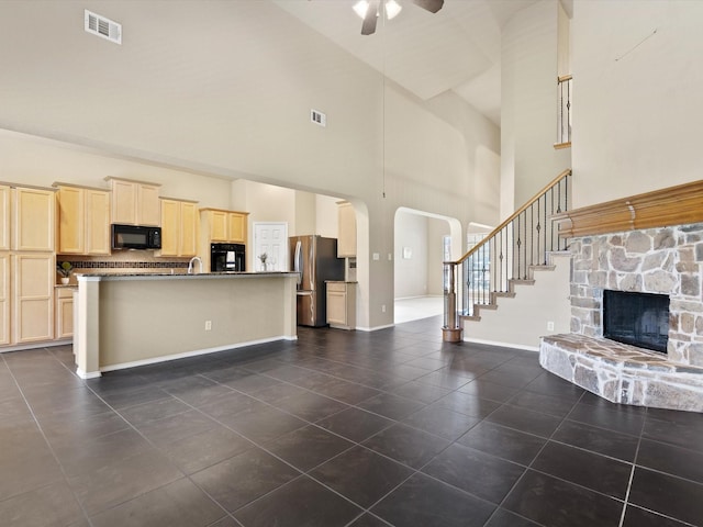 kitchen with a stone fireplace, high vaulted ceiling, light brown cabinets, ceiling fan, and black appliances