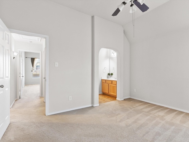 unfurnished bedroom featuring ceiling fan, ensuite bathroom, vaulted ceiling, and light carpet