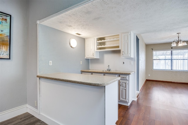 kitchen featuring sink, decorative light fixtures, dark hardwood / wood-style floors, kitchen peninsula, and white cabinets