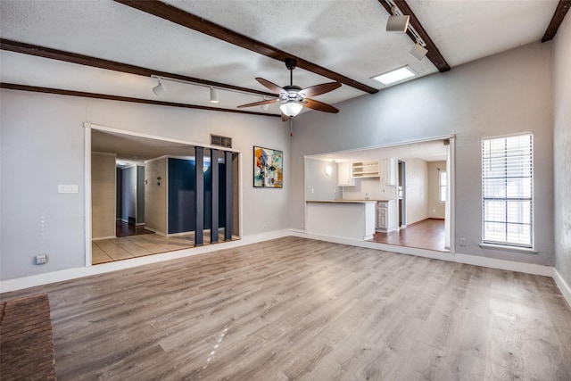 unfurnished living room featuring vaulted ceiling with beams, track lighting, light hardwood / wood-style floors, and a textured ceiling