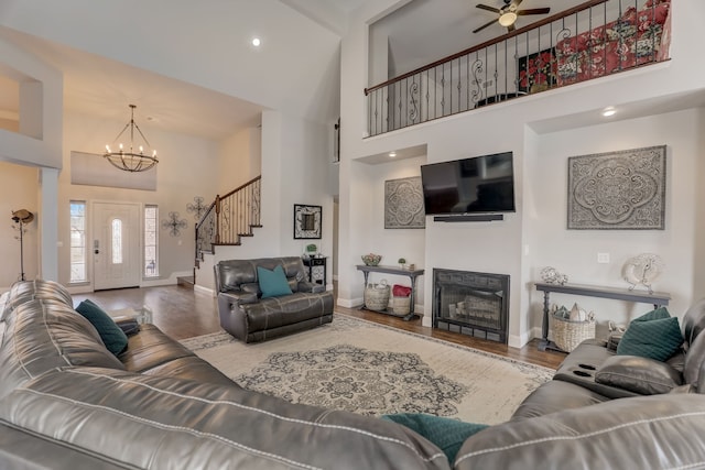 living room with wood-type flooring, ceiling fan with notable chandelier, and a high ceiling