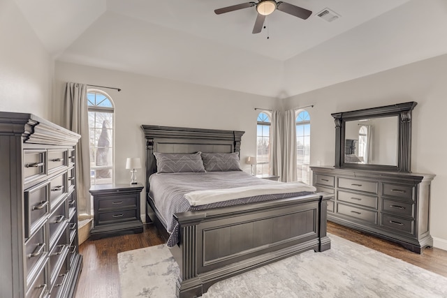 bedroom with ceiling fan, a tray ceiling, dark hardwood / wood-style flooring, and multiple windows