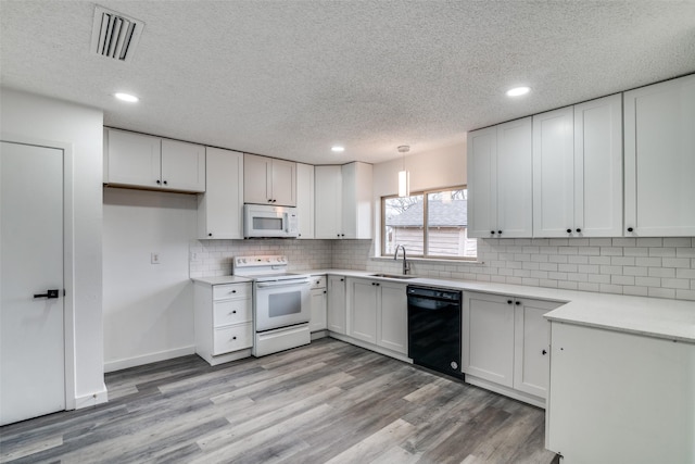 kitchen featuring white cabinetry, sink, light wood-type flooring, hanging light fixtures, and white appliances