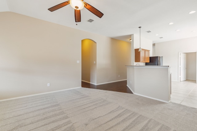 unfurnished living room featuring vaulted ceiling, light carpet, and ceiling fan