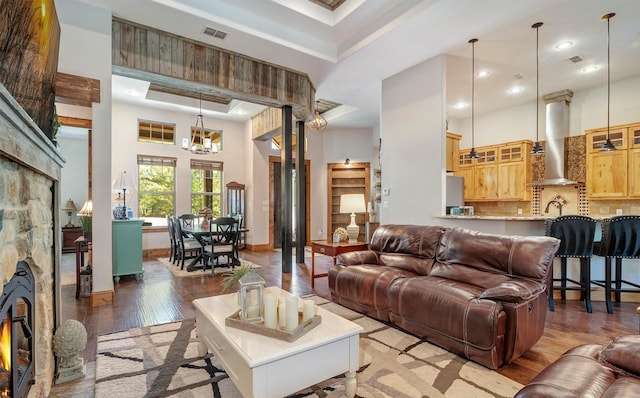 living room featuring a stone fireplace, wood-type flooring, sink, a chandelier, and a high ceiling