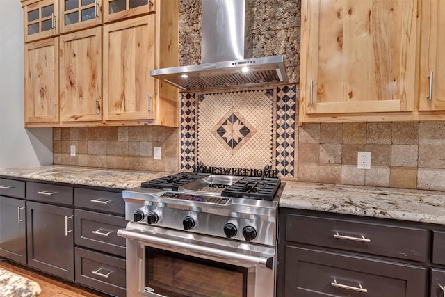 kitchen featuring stainless steel range, light stone countertops, dark brown cabinets, and wall chimney range hood