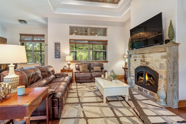 living room with light wood-type flooring, a wealth of natural light, a fireplace, and a tray ceiling