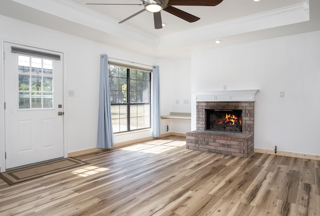 unfurnished living room with crown molding, a raised ceiling, light hardwood / wood-style floors, and a brick fireplace