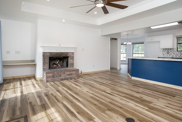 2048 County Road 3540, Hawkins, TX 75765 - unfurnished living room with light wood-style flooring, ceiling fan with notable chandelier, a brick fireplace, ornamental molding, and a raised ceiling