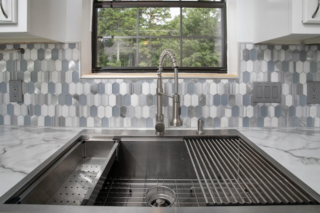 interior space featuring light stone countertops, sink, white cabinets, and decorative backsplash