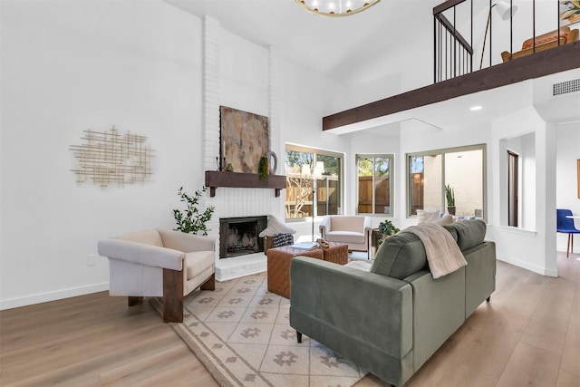 living room featuring an inviting chandelier, a fireplace, a high ceiling, and light hardwood / wood-style flooring