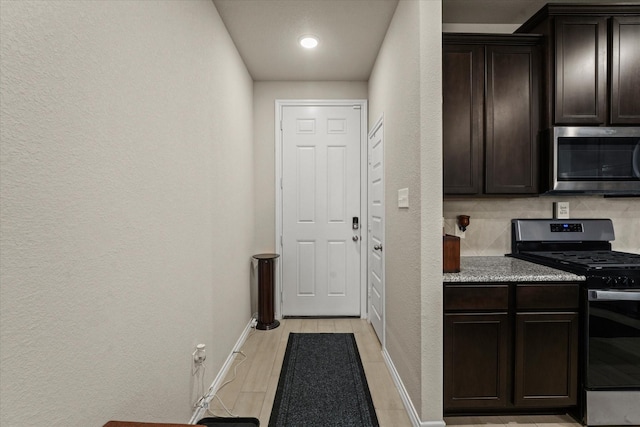 kitchen featuring stainless steel appliances, a textured wall, baseboards, and dark brown cabinetry