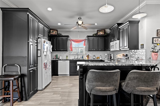 kitchen featuring stone countertops, sink, a kitchen breakfast bar, kitchen peninsula, and white appliances