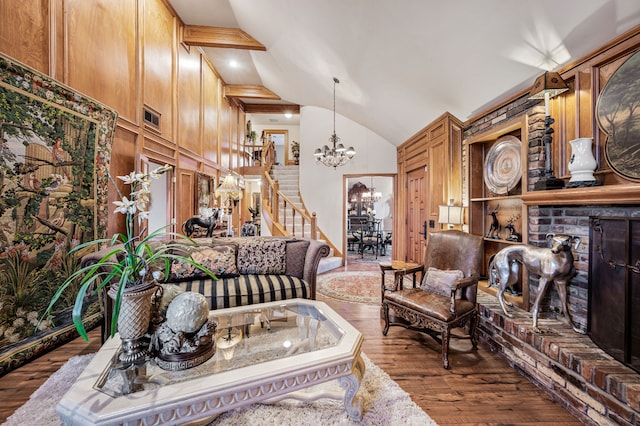 living room with dark wood-type flooring, wood walls, a brick fireplace, a notable chandelier, and beam ceiling