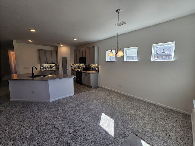 kitchen with sink, backsplash, hanging light fixtures, dark carpet, and a center island with sink